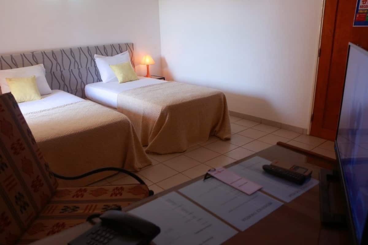 A hotel room with two beds, a desk with a computer and paperwork, and a reception sign.
