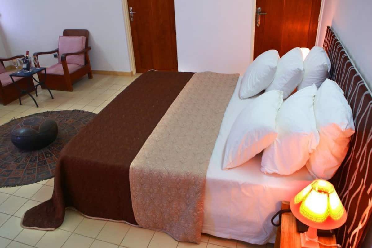 A neatly arranged bedroom with a bed, pillows, a bedside lamp, a rug, and two chairs.