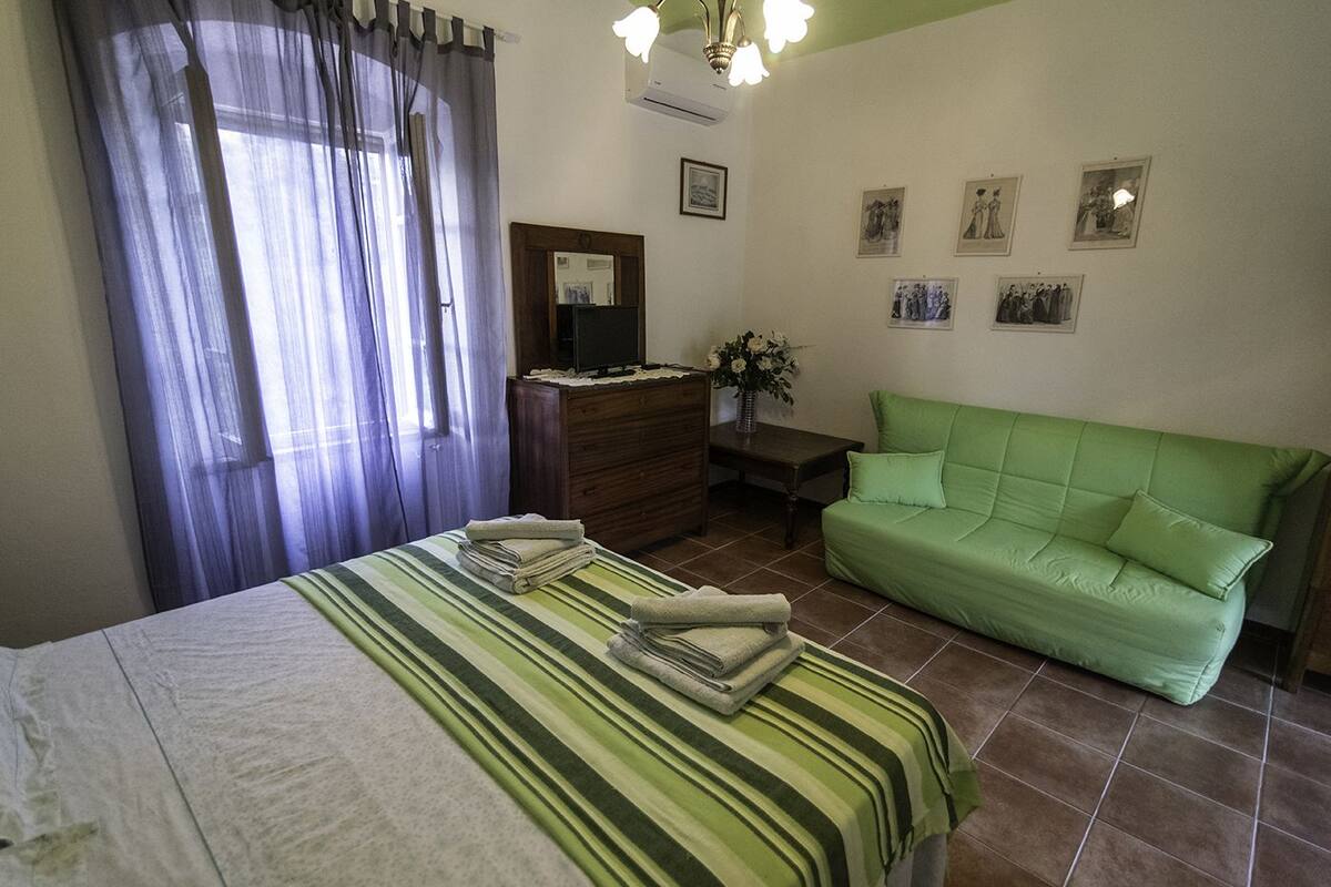 Un dormitorio con cama, sofá verde, cómoda y espejo.