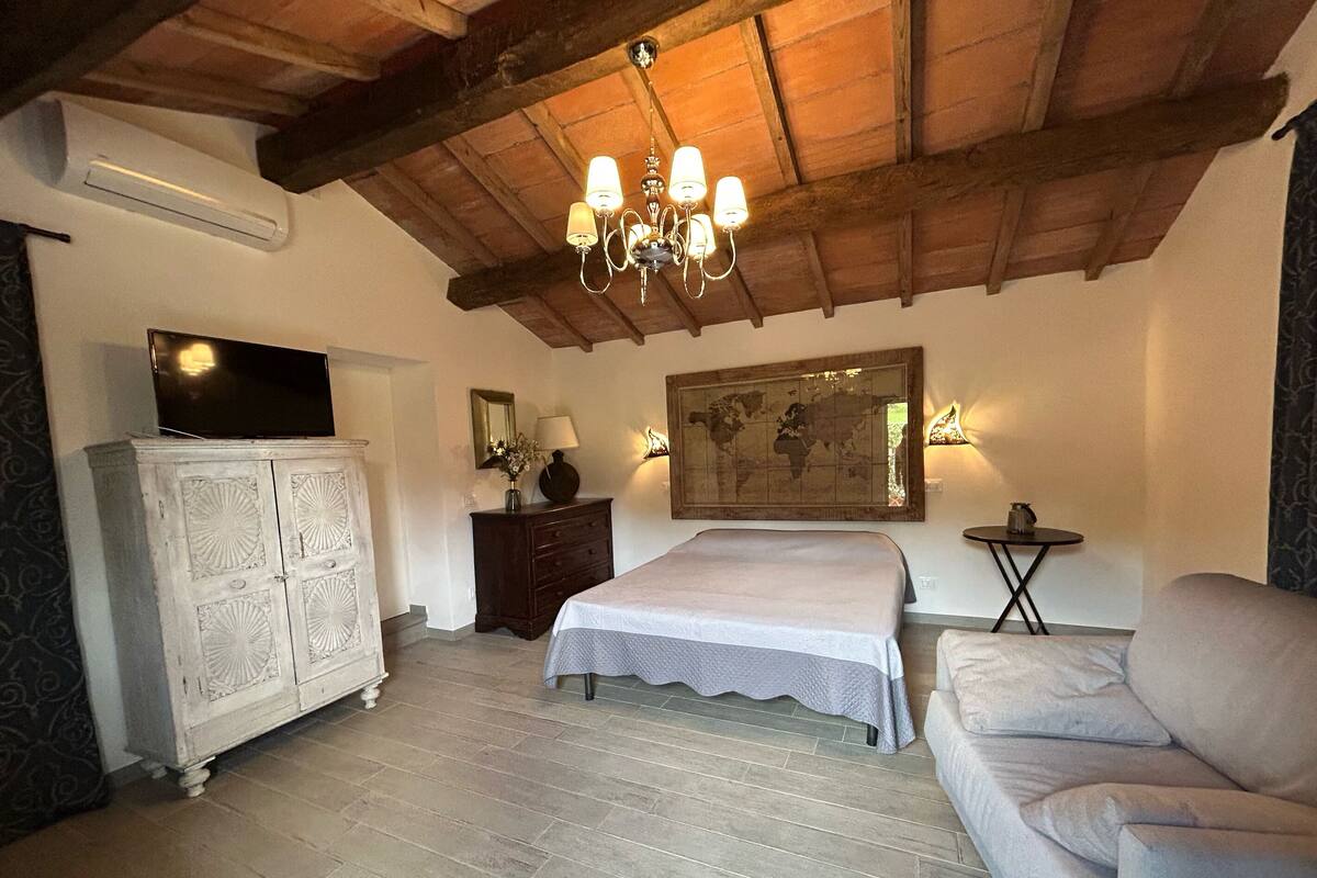 Un dormitorio con una cama grande, un aparador, un televisor, un mapa mundial y una pequeña mesa con lámpara.