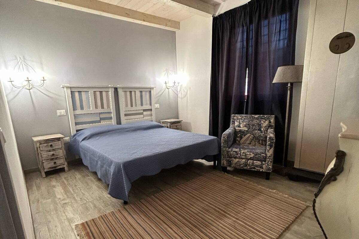 Un dormitorio con cama, una silla, una mesita de noche y una lámpara.