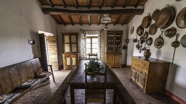 Une salle à manger rustique avec une table et des bancs en bois, un buffet en bois et un mur décoré de casseroles et de poêles suspendues.
