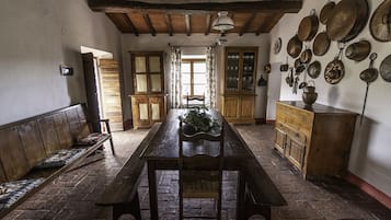 Ein rustikaler Essraum mit Holztisch und Bänken, einem Holzschrank und einer Wand, die mit hängenden Töpfen und Pfannen dekoriert ist.