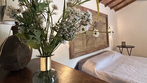 Une pièce avec un plafond en bois, un lit recouvert d’une courtepointe blanche, une petite table ornée d’un vase de fleurs et une carte encadrée accrochée au mur.