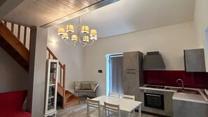 Une cuisine moderne dotée d’un four encastré, un coin repas avec une table et des chaises blanches, et un canapé rouge.