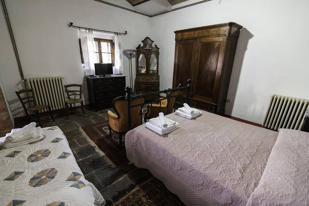 Un dormitorio con cama, cómoda, silla, espejo y radiador.