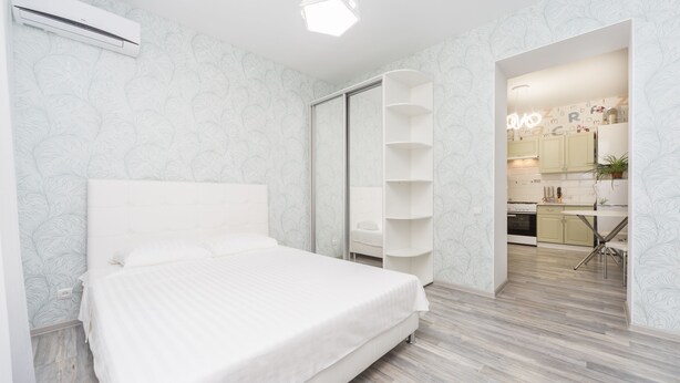 Un dormitorio con cama, armario y cocina visible a través de una puerta abierta.