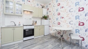 Una cocina con armarios verde claro, estufa blanca y refrigerador blanco. Hay una mesa blanca con dos sillas y una planta en maceta sobre la encimera.