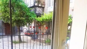 Vista desde una ventana con una verja de metal, plantas en macetas y un edificio con balcones.