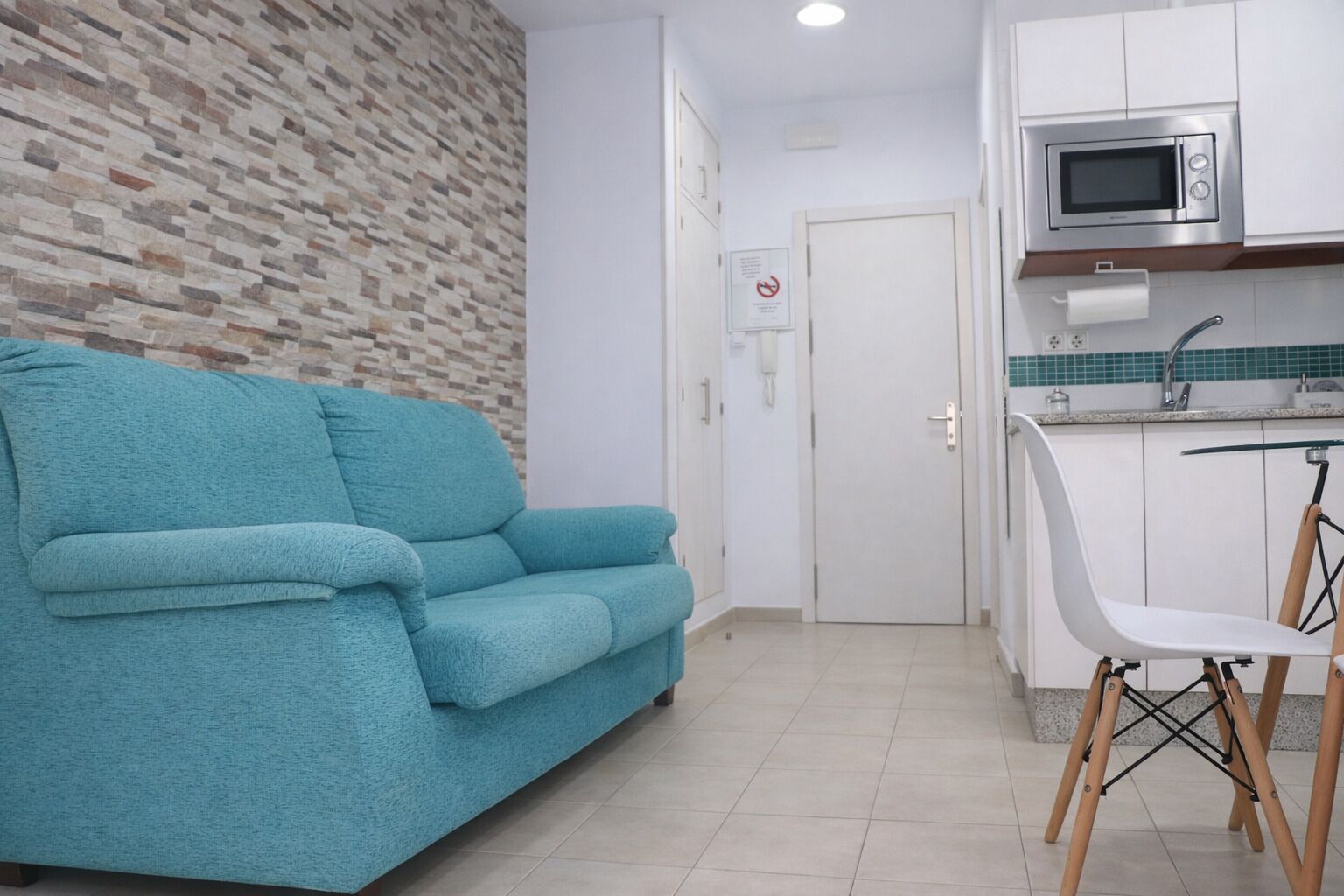 A living room with a teal sofa, a kitchen with white cabinets, and a microwave.