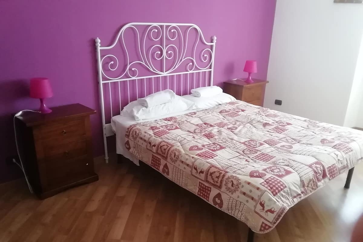 A bedroom with a bed, wooden nightstands, and a purple wall.