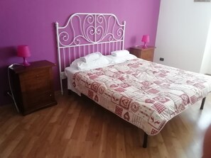 Quarto com cama, mesas de cabeceira de madeira e parede roxa.