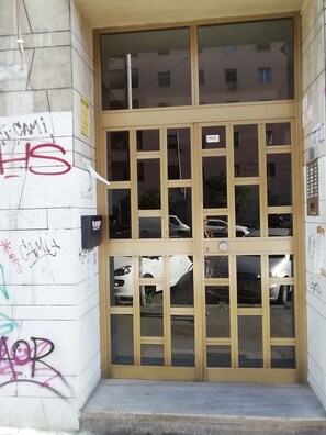 A building entrance with a glass door and windows, surrounded by walls with graffiti. - Porta Maggiore Guest House (Rome)