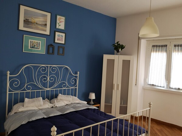 Quarto com cama, guarda-roupa, janela com cortinas e quadros nas paredes.