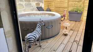 Een zebra staat naast een jacuzzi op een houten terras.