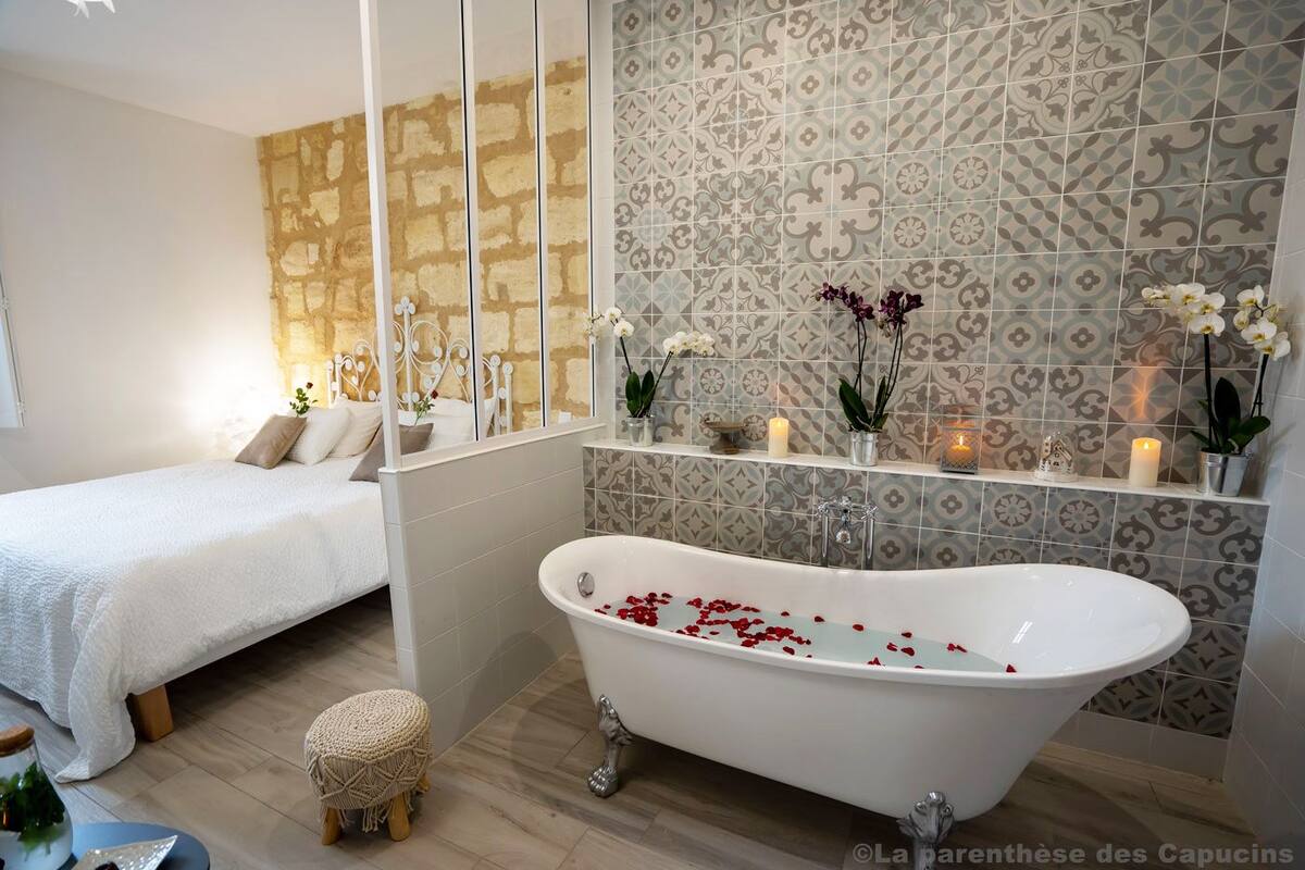Un baño con una bañera independiente, zona de ducha y cama con cabecero blanco.