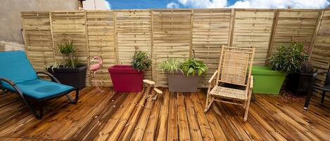 A wooden deck with a blue lounge chair, a red planter, and a wooden chair.