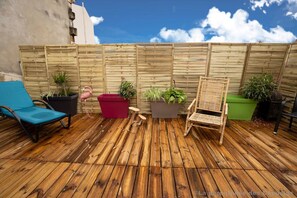 Une terrasse en bois avec un fauteuil de jardin bleu, un pot de fleurs rouge et une chaise en bois.