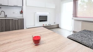 Eine moderne Küche mit weißen Schränken, einem eingebauten Backofen und einem flachbildfernseher an der Wand.
