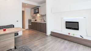 Eine moderne Küche mit Holzausstattung, einem eingebauten Backofen und einer Mikrowelle. Es gibt einen Essbereich mit Tisch und Stühlen, sowie einen an der Wand montierten Fernseher.