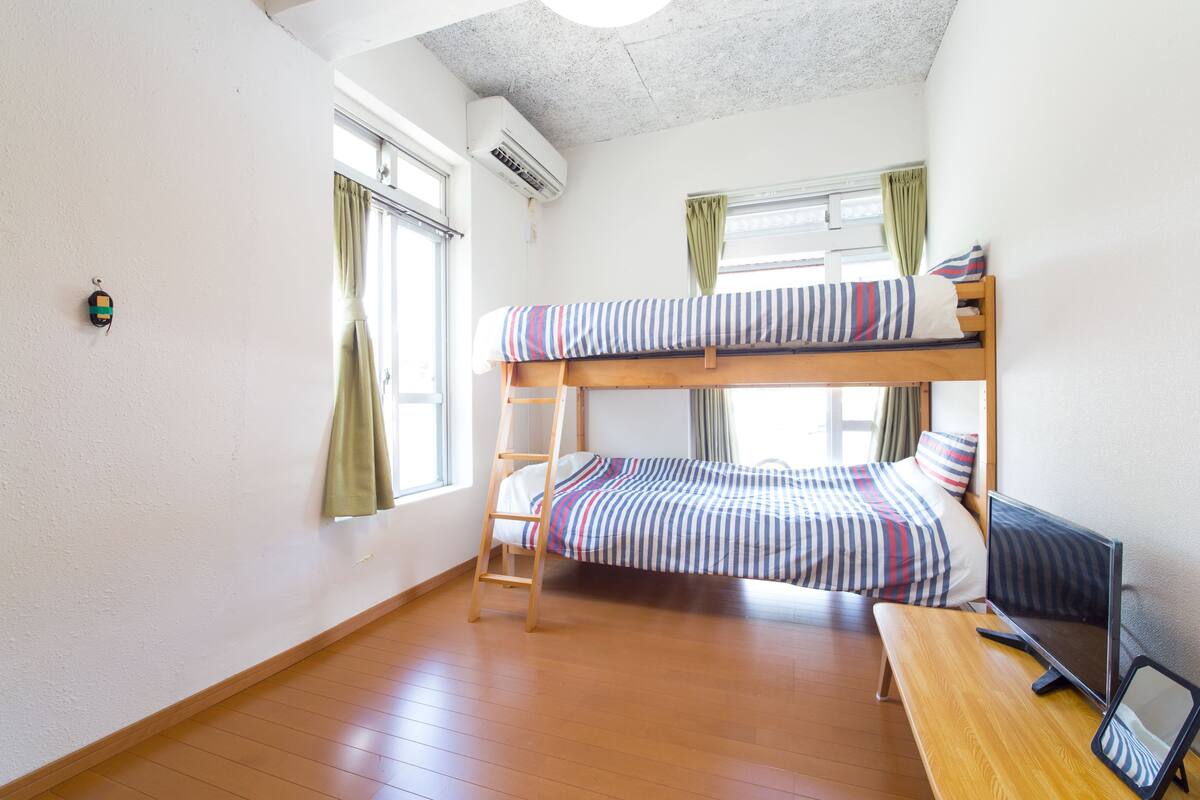 A bunk bed room with a wooden ladder, a desk, and a computer.