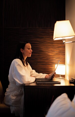 A person seated at a wooden desk with a lamp, in a room with dark wood paneling. - Garni Hotel Aleksandar (Novi Sad)