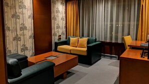 A modern hotel room with a sofa, a small table, a desk, and a chair. - Garni Hotel Aleksandar (Novi Sad)