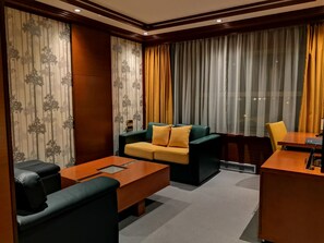 A modern hotel room with a sofa, a small table, a desk, and a chair. - Garni Hotel Aleksandar (Novi Sad)