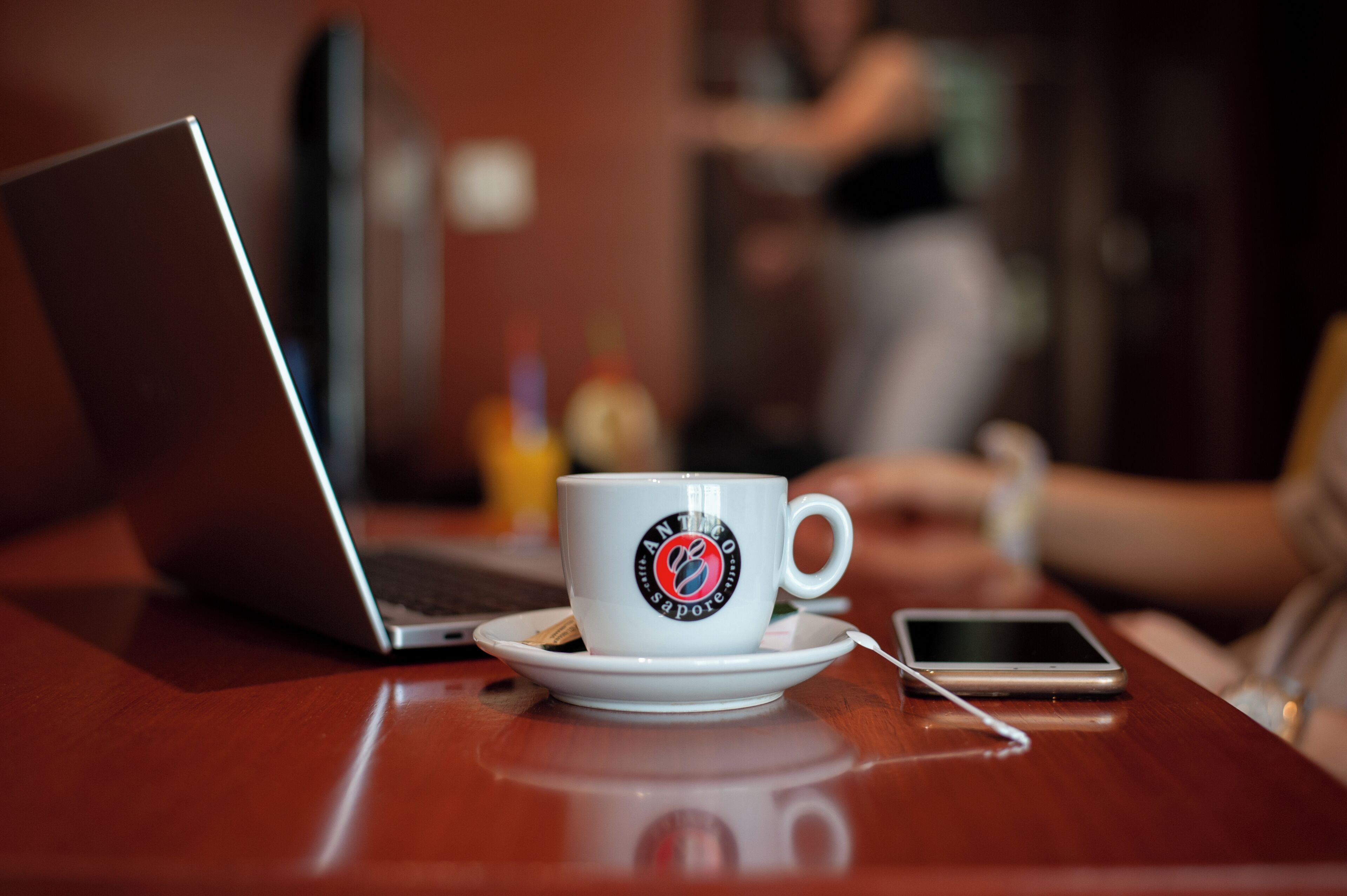 A laptop, a smartphone, and a cup with a logo on a wooden table.
