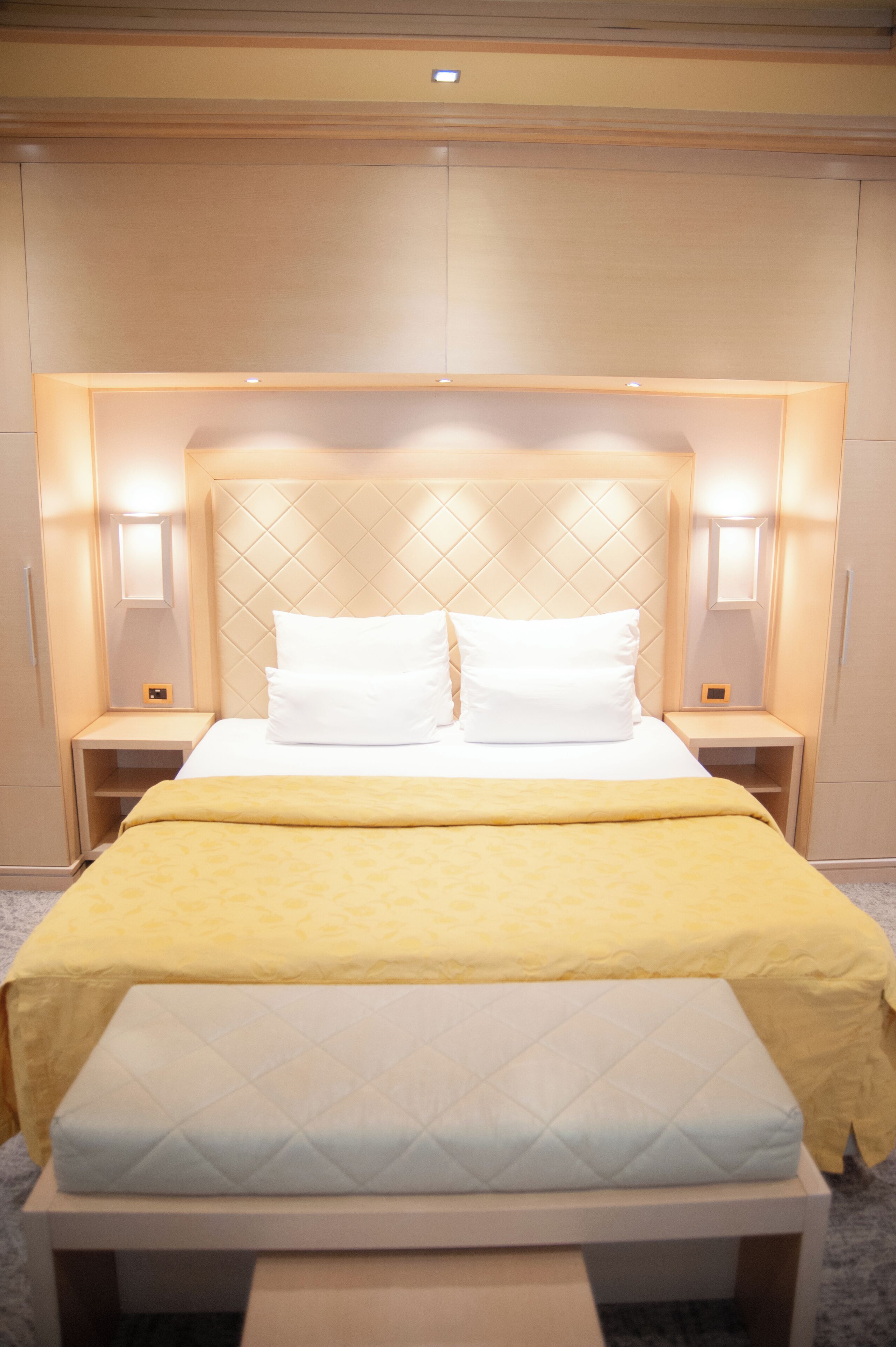 A hotel room with a bed, bedside tables, and a headboard with built-in lighting.