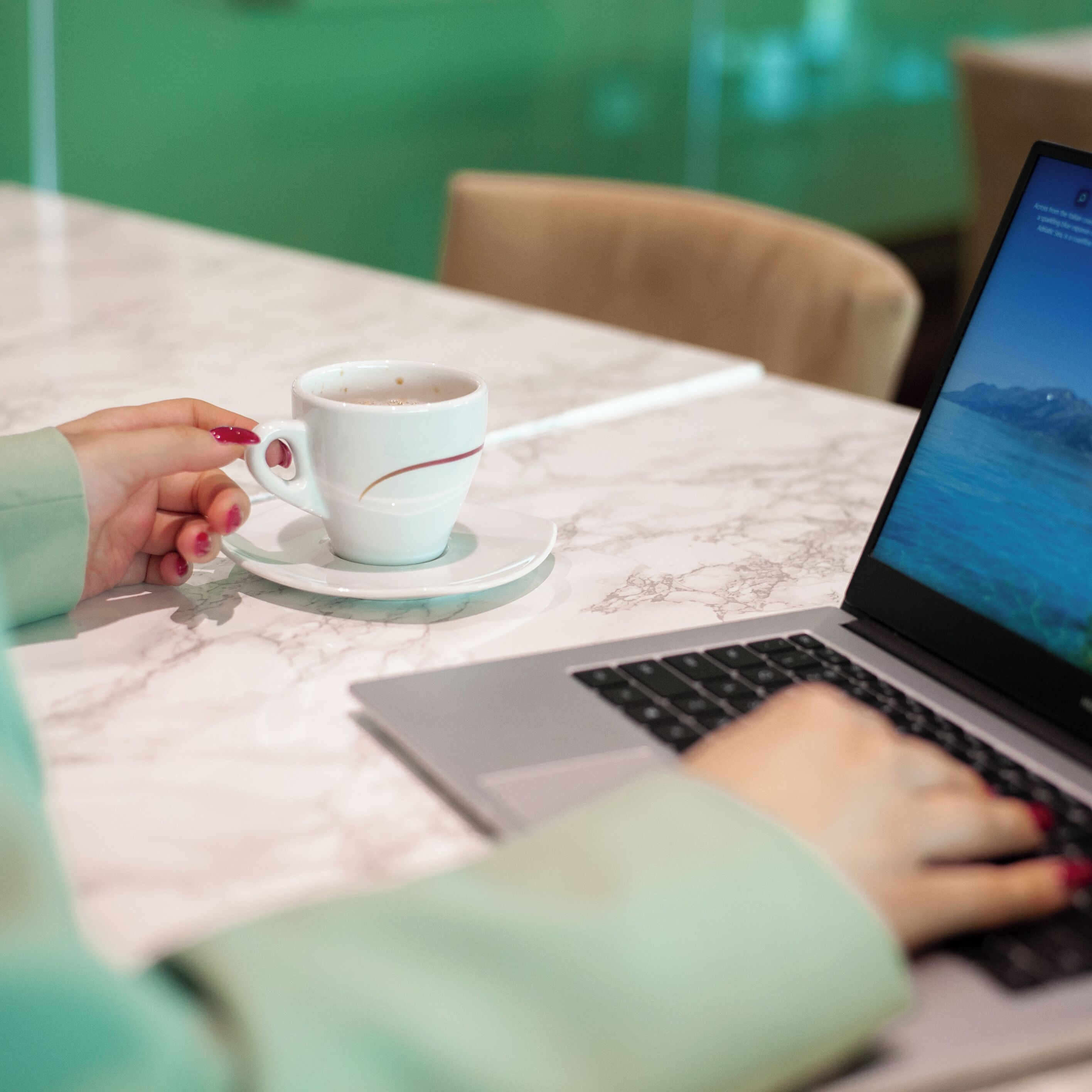 Una persona usando una computadora portátil a una mesa con una taza de café.