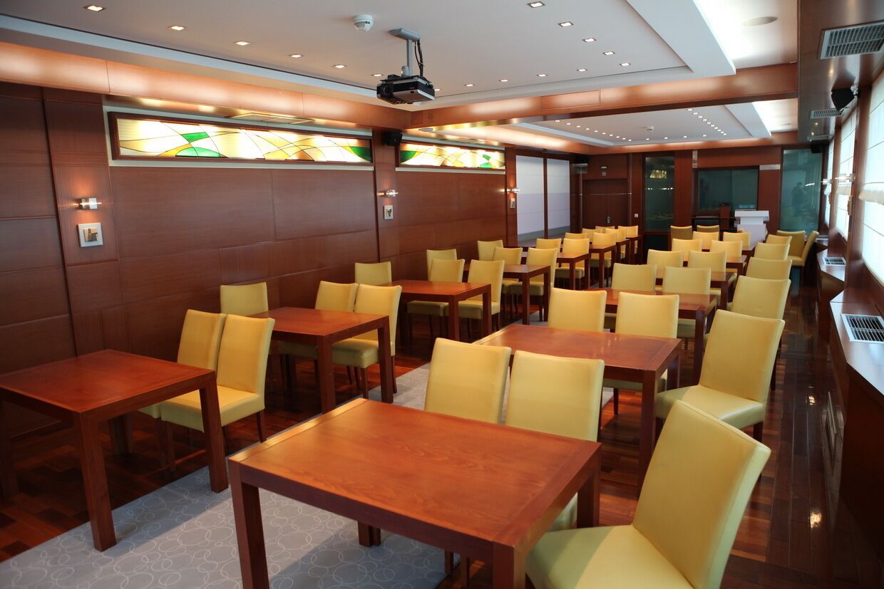 A hotel conference room with multiple tables and chairs, a projector, and a large window.