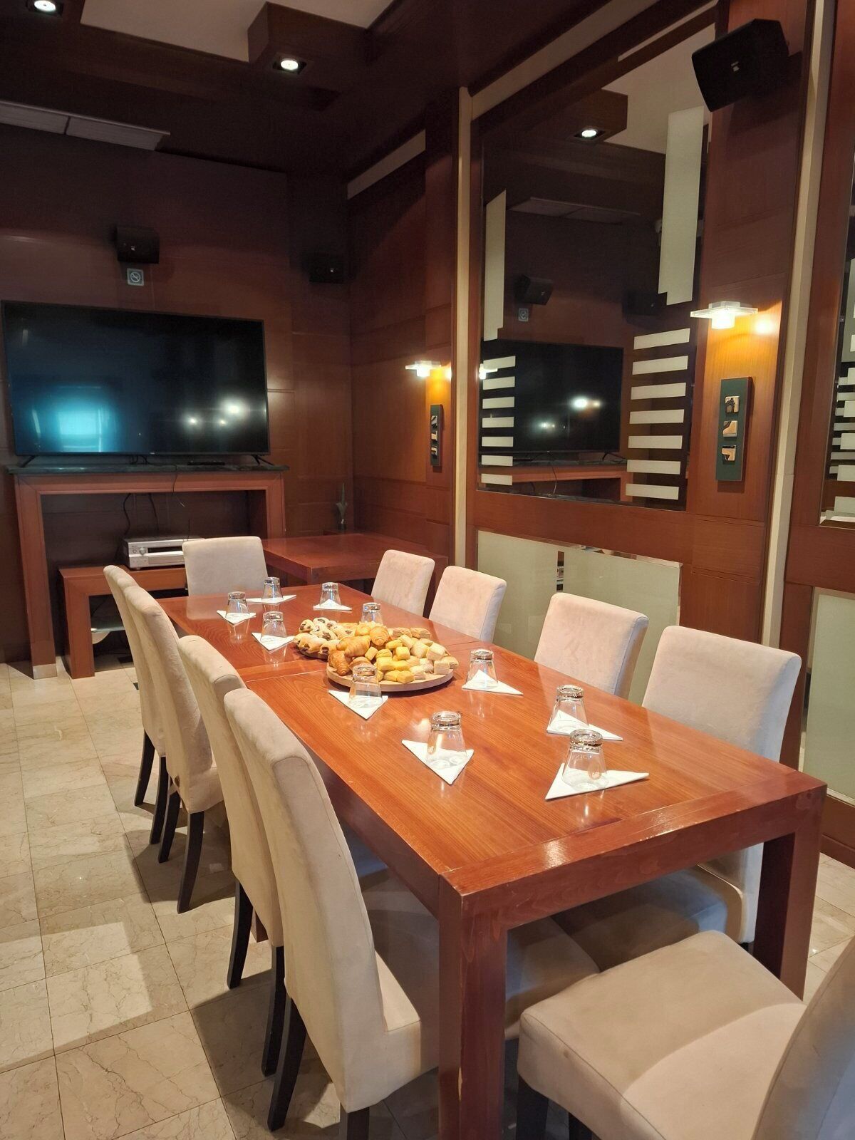 Een vergaderzaal met een lange houten tafel, witte stoelen, een flatscreen televisie en een buffet met gebak.