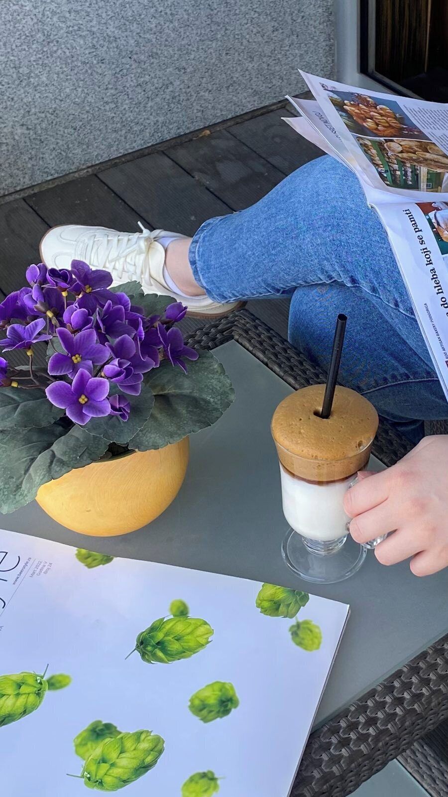 Une personne tenant un verre avec une paille, assise à une table avec une plante en pot et un menu.