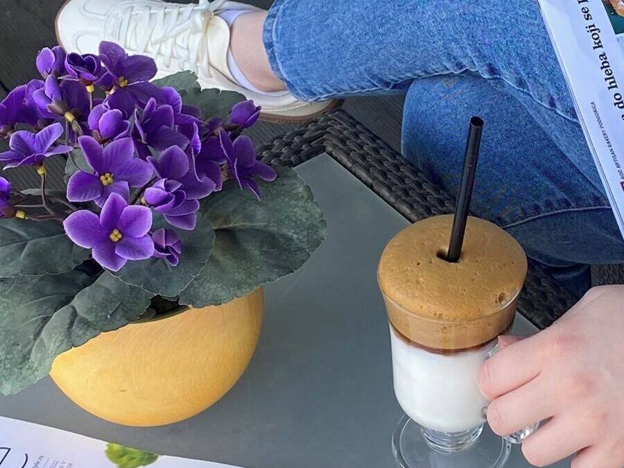 A person holding a drink with a straw, seated at a table with a potted plant and a menu.
