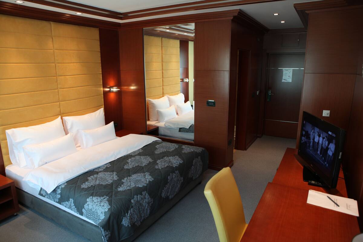 A hotel room with a large bed, a television, a desk, and a mirror.
