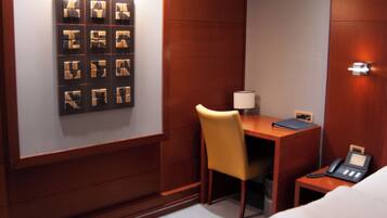 Ein Hotelzimmer mit einem Bett, einem Schreibtisch, einem Stuhl und einem an der Wand befestigten Telefon.