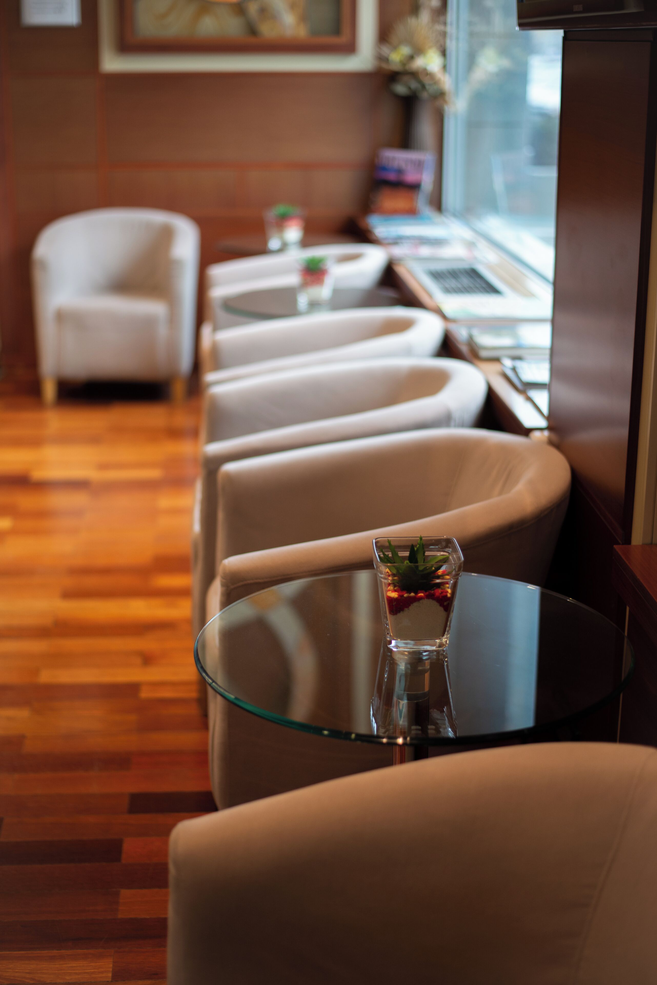 A hotel room with a seating area featuring a glass table with a plant and a laptop.