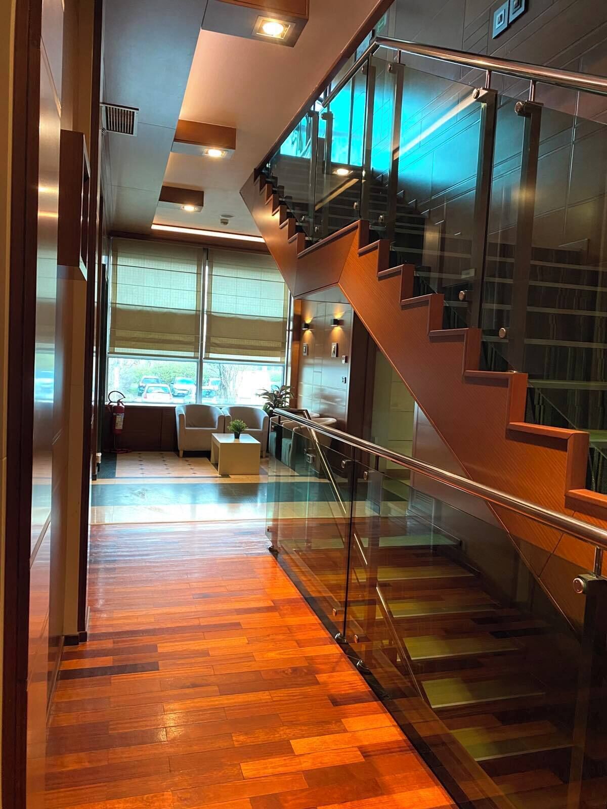 A modern interior with a wooden floor, a glass staircase, and a seating area with a view of the outdoors.