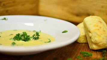 Plat blanc amb sopa groga adornada amb herbes verdes, acompanyat de dues peces de pa sobre una superfície de fusta.