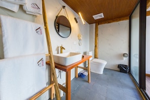 A bathroom with a wooden vanity, a round mirror, a white sink, and a toilet.