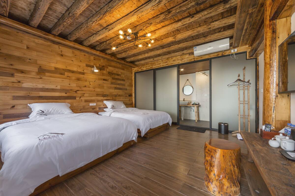 A wooden cabin-style room with two beds, a wooden ceiling, a hanging light fixture, and a wooden stool.