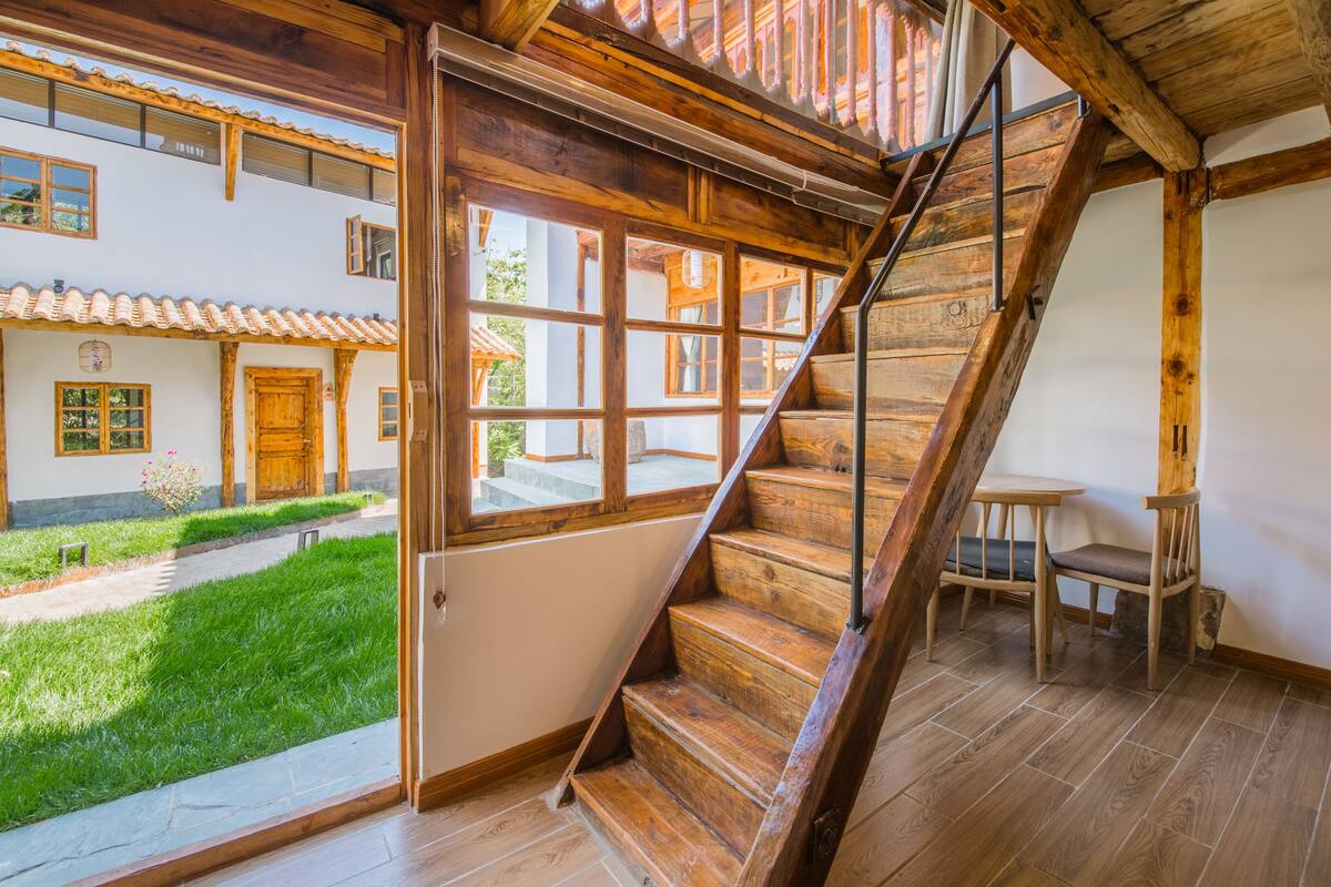A wooden staircase leading to an upper floor with a view of a garden and a building with a tiled roof.
