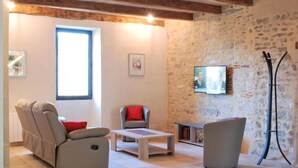 A cozy living room with a stone wall, a flat-screen TV, a sofa, a chair, and a coffee table. - Gite Le Roucayral– Superb view over St Cirq Lapopie – 2 air-conditioned bedrooms (Tour de Faure)