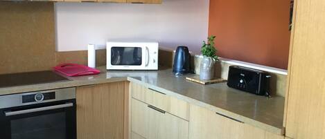 A modern kitchen with wooden cabinets, a built-in oven, a microwave, a kettle, and a toaster.