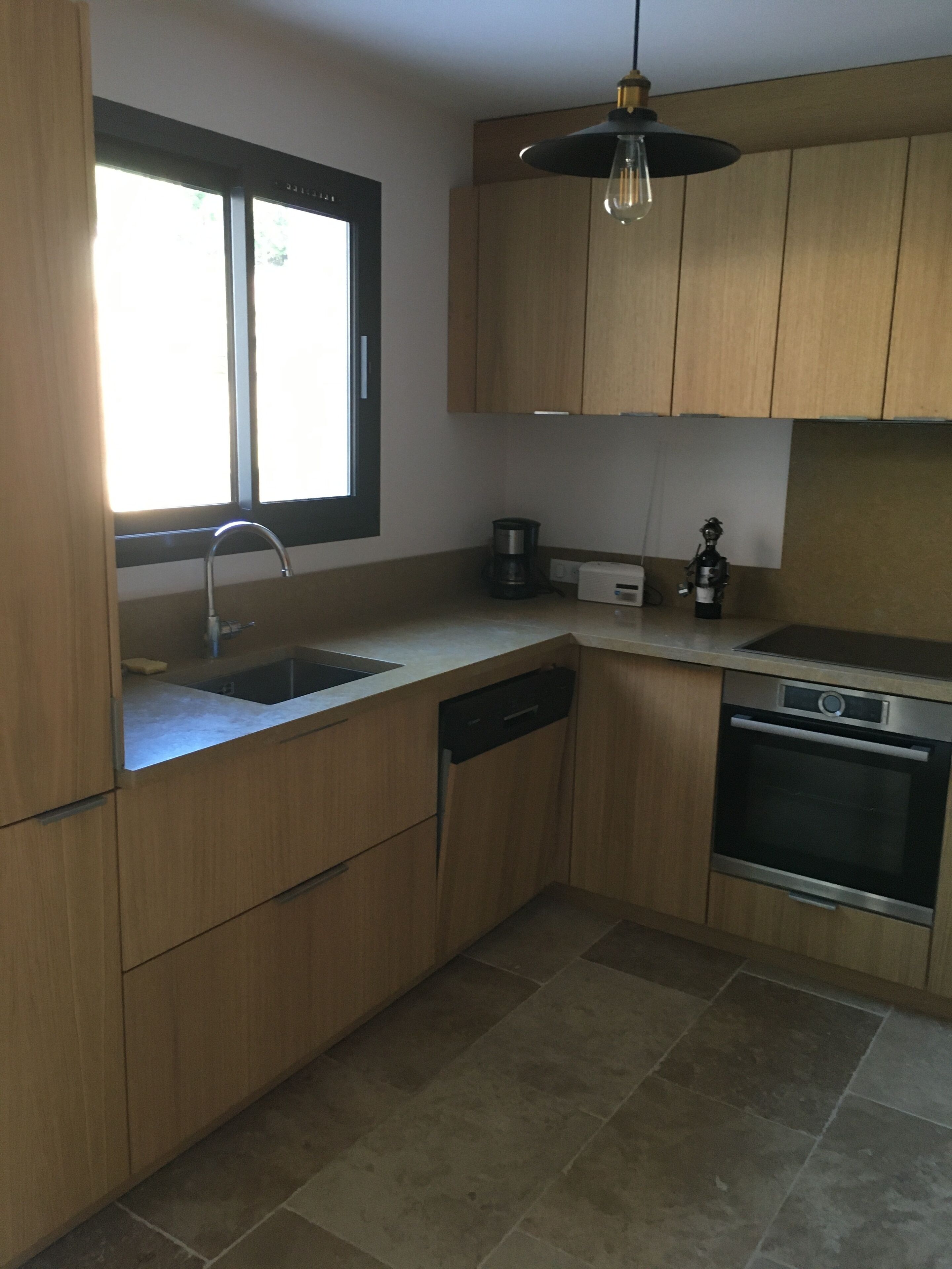 A modern kitchen with wooden cabinets, a stainless steel sink, a dishwasher, a coffee maker, and an oven.