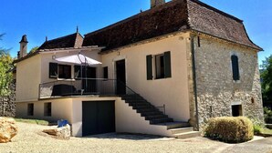 A two-story stone house with a balcony, a staircase, and a covered outdoor seating area. - Gite Le Roucayral– Superb view over St Cirq Lapopie – 2 air-conditioned bedrooms (Tour de Faure)
