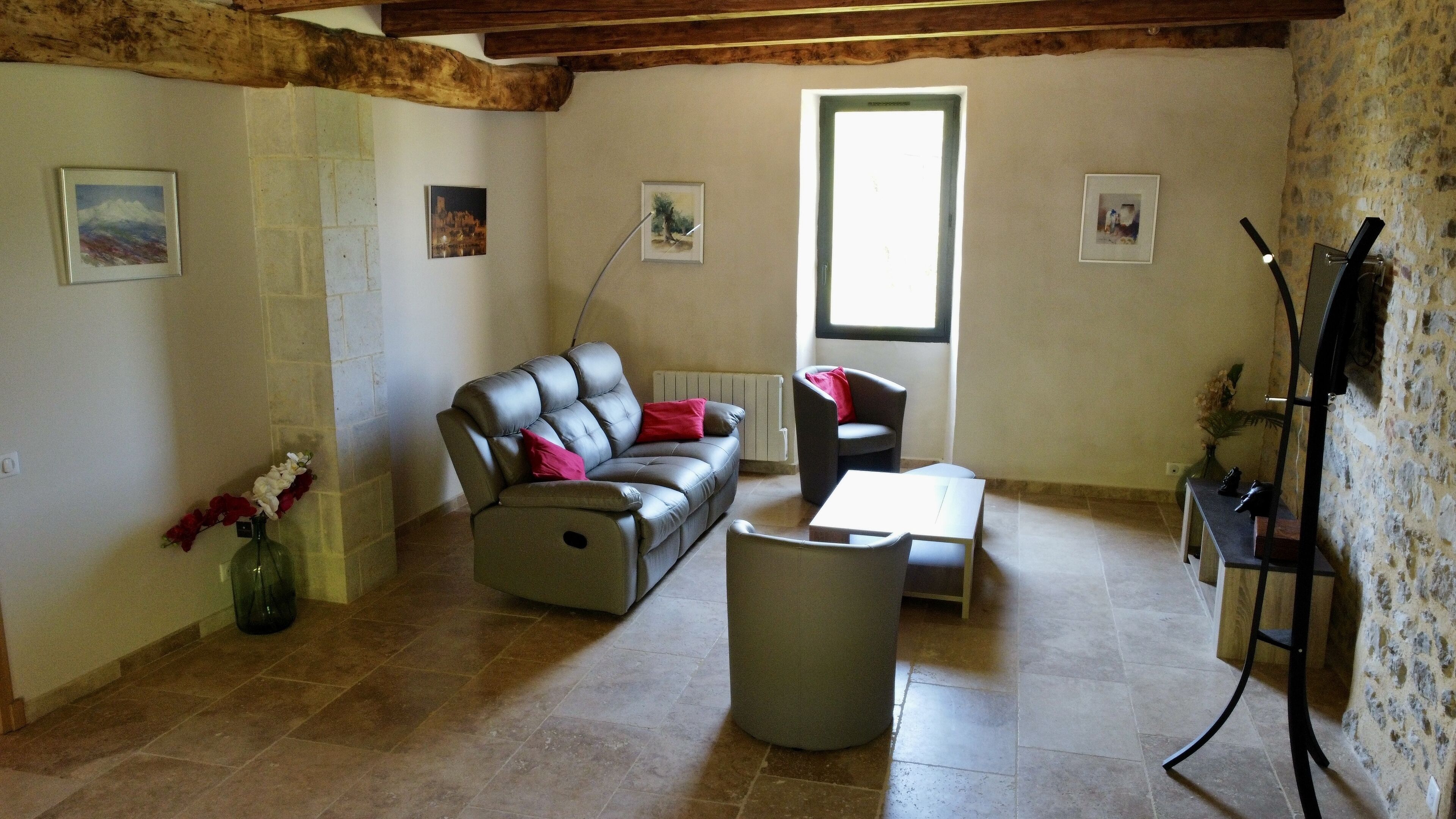A living room with a sofa, armchair, and a coffee table. There is a radiator, a window, and a stone wall.