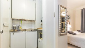 A compact hotel room with a kitchenette, a bed with dark bedding, and a large mirror. - Go Happy Home Apartment Mikonkatu 18 (Helsinki)