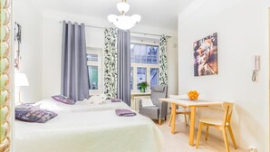 A hotel room with two beds, a desk, a chair, a table, a lamp, a picture on the wall, and a window with curtains. - Go Happy Home Apartment Mikonkatu 18 (Helsinki)